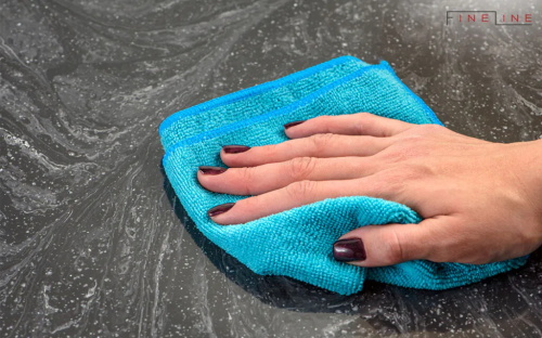 Hand cleaning dark countertop with blue microfiber cloth
