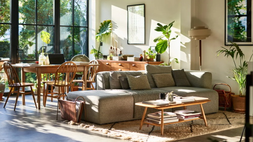 Bright modern living room with large windows, sectional sofa, and dining area