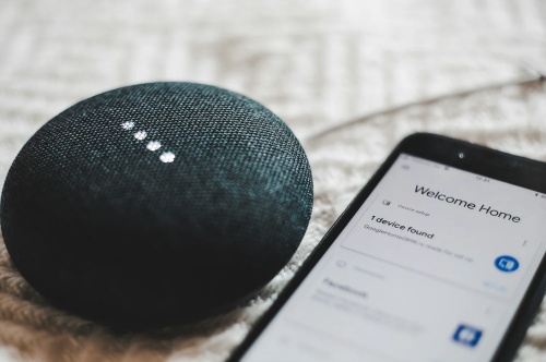 A smart speaker sits next to a phone displaying the Welcome Home setup screen